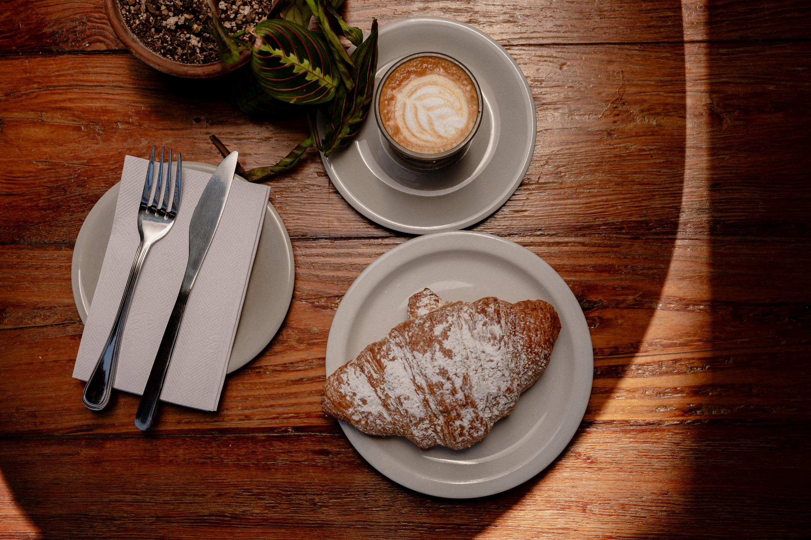 A croissant and coffee served on ceramic plates at Kinfolx