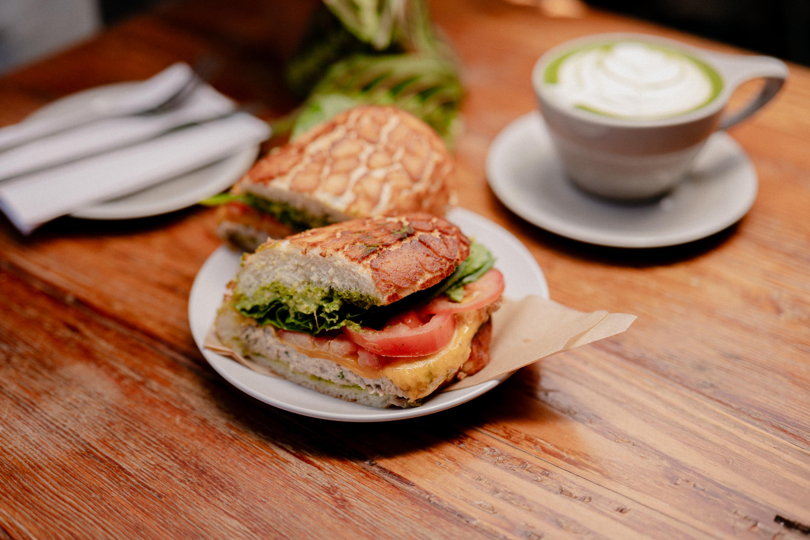 A sandwich with greens and tomato beside a matcha drink at Kinfolx